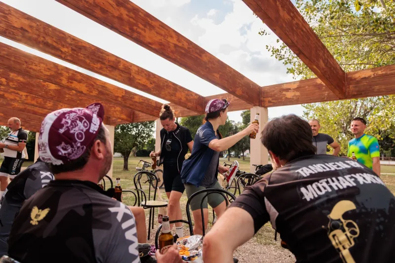 Riders raising their glasses at a table under a wooden pergola